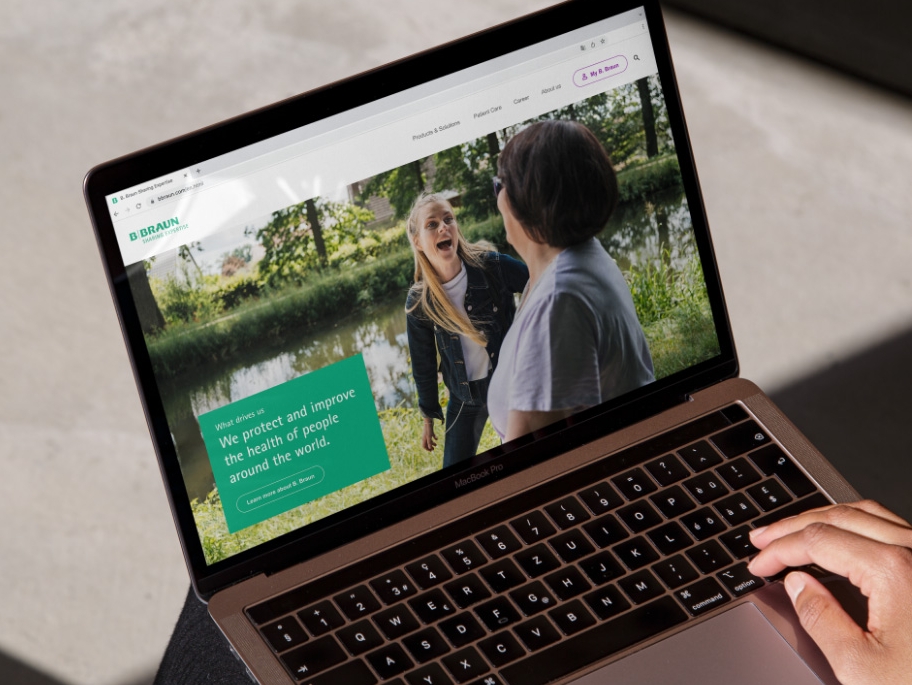En bærbar computer med B. Brauns websted åbent og en hånd hvilende nederst til højre på den bærbare computer. 