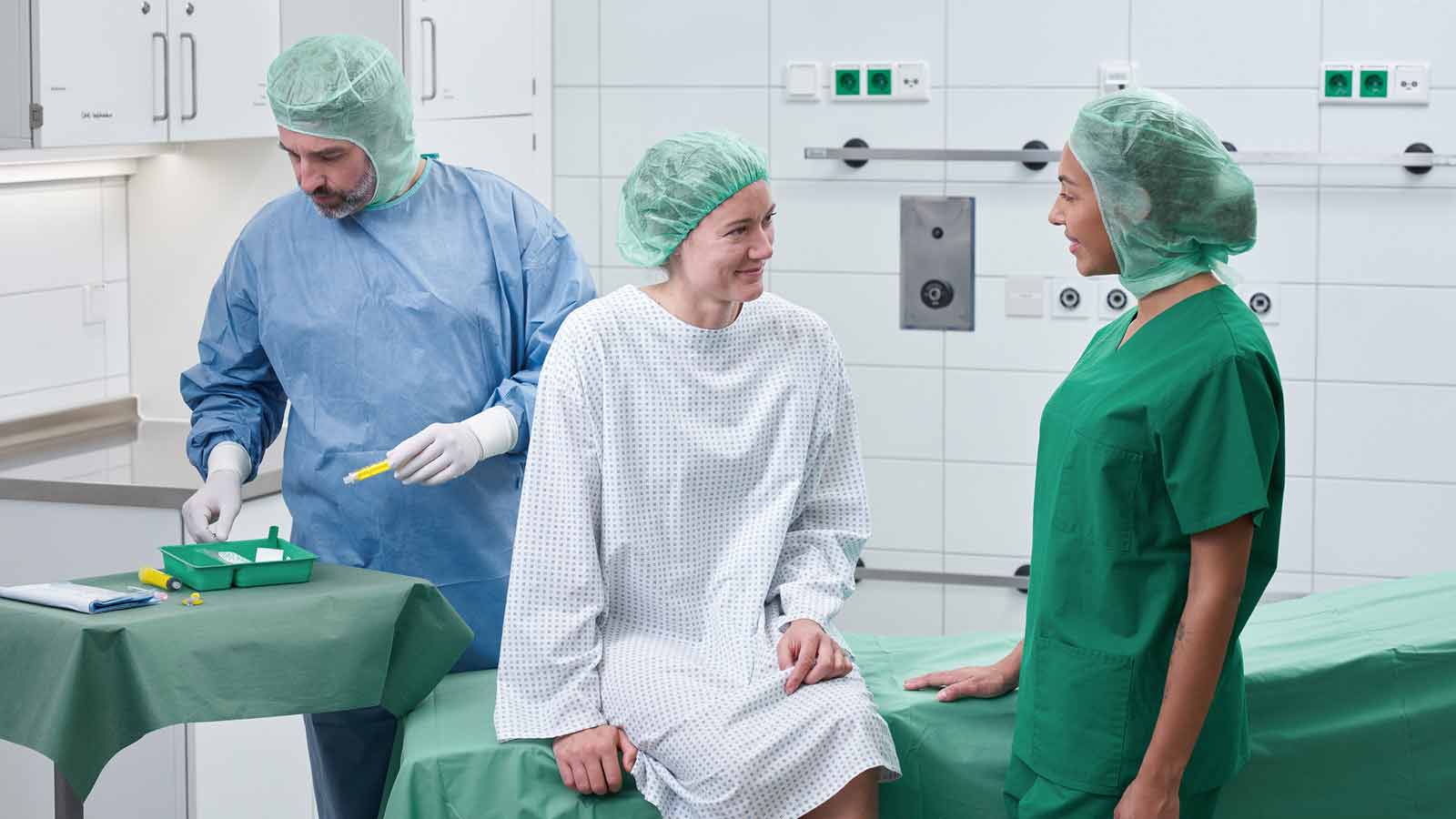 Hospitalsstue med medicinsk udstyr, der viser en patientseng, monitoreringsudstyr og kliniske forsyninger. Sundhedspersonale i medicinsk uniform forbereder sig på patientpleje.