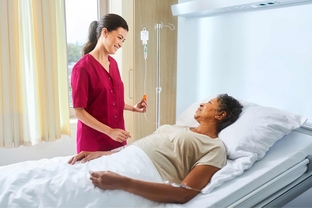 Sygeplejerske med ecoflac plus på et infusionsstativ taler med en patient, der ligger i sengen