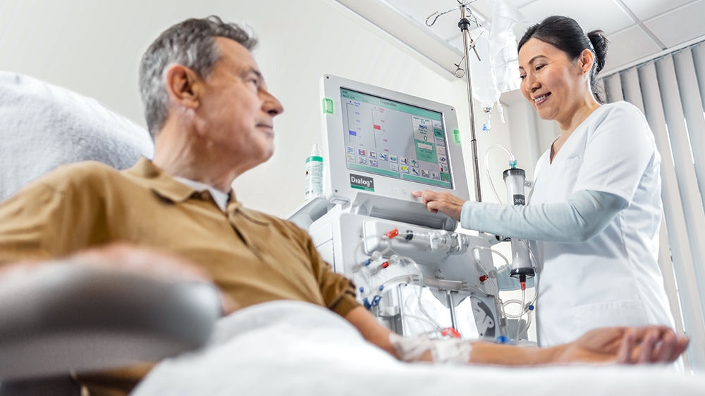Patient får dialyse, i baggrunden en sygeplejerske, der håndterer en dialog + maskine