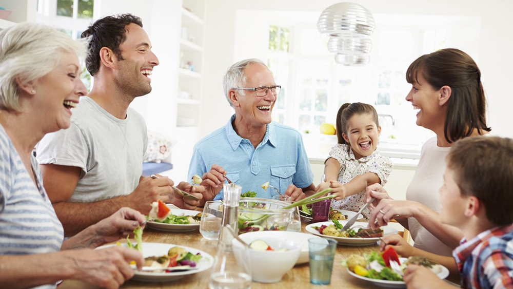 En familie sidder ved bordet og spiser og griner