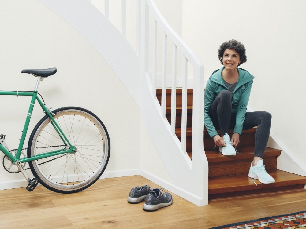 Til højre sidder en kvinde på trappen og binder sine sko, til venstre er der en cykel og endnu et par sko